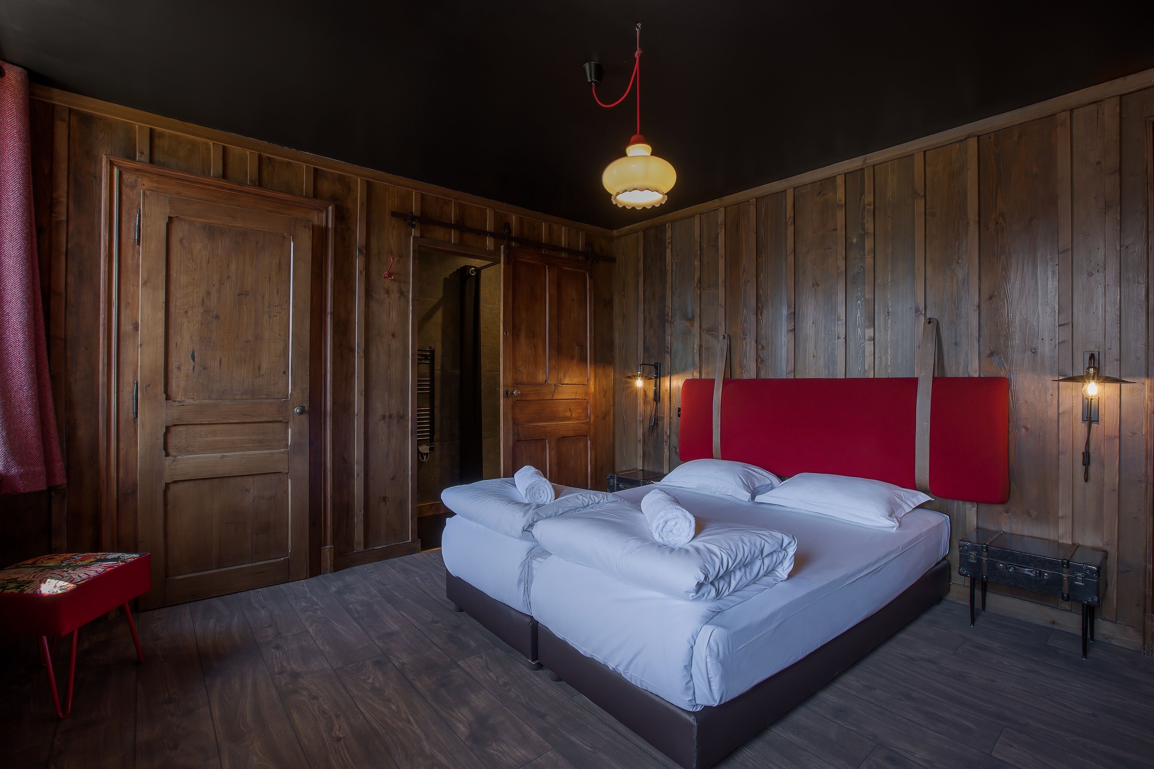 Quarto com painéis de madeira, uma cama e uma luminária pendente. A cabeceira é vermelha.