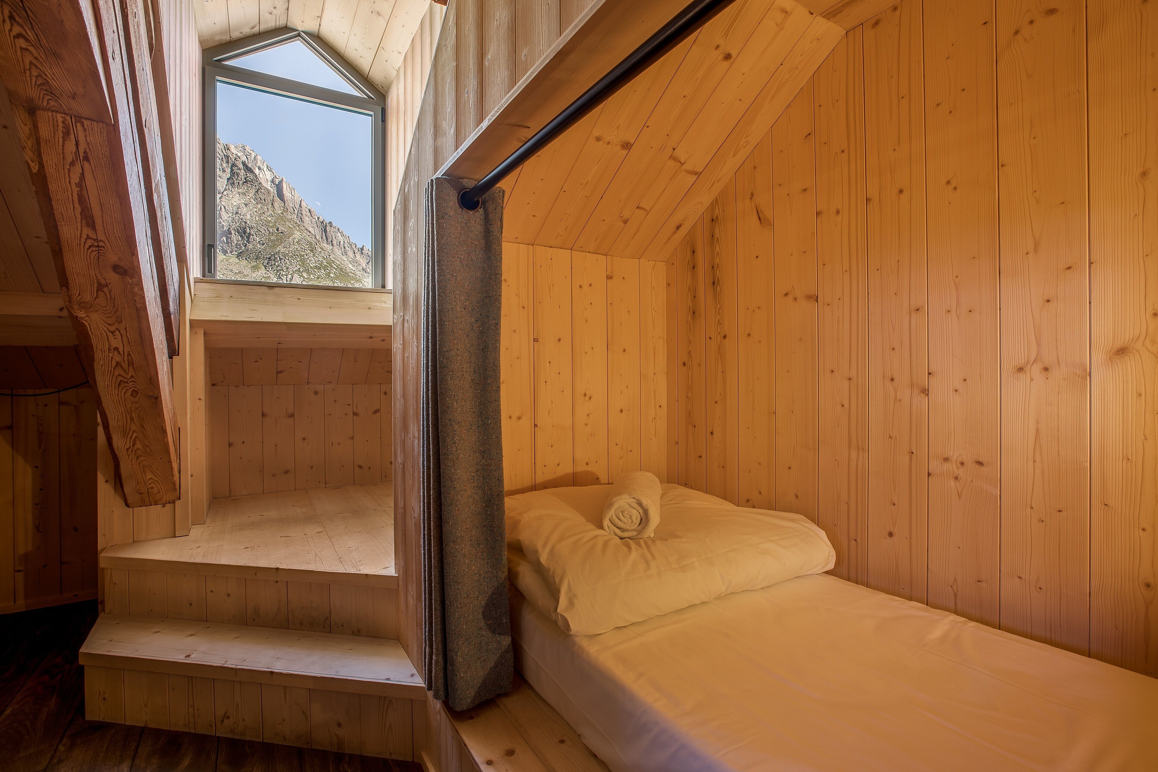 A wooden cabin room with a bed, a window, and a staircase.