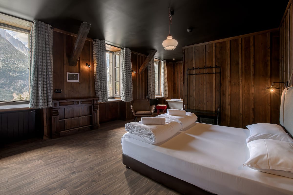 Une pièce en bois avec un lit, une chaise, un bureau et une vue sur les montagnes.