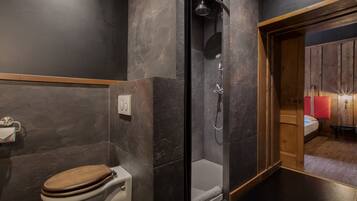 A modern bathroom with a shower, toilet, and a wooden door leading to a bedroom.
