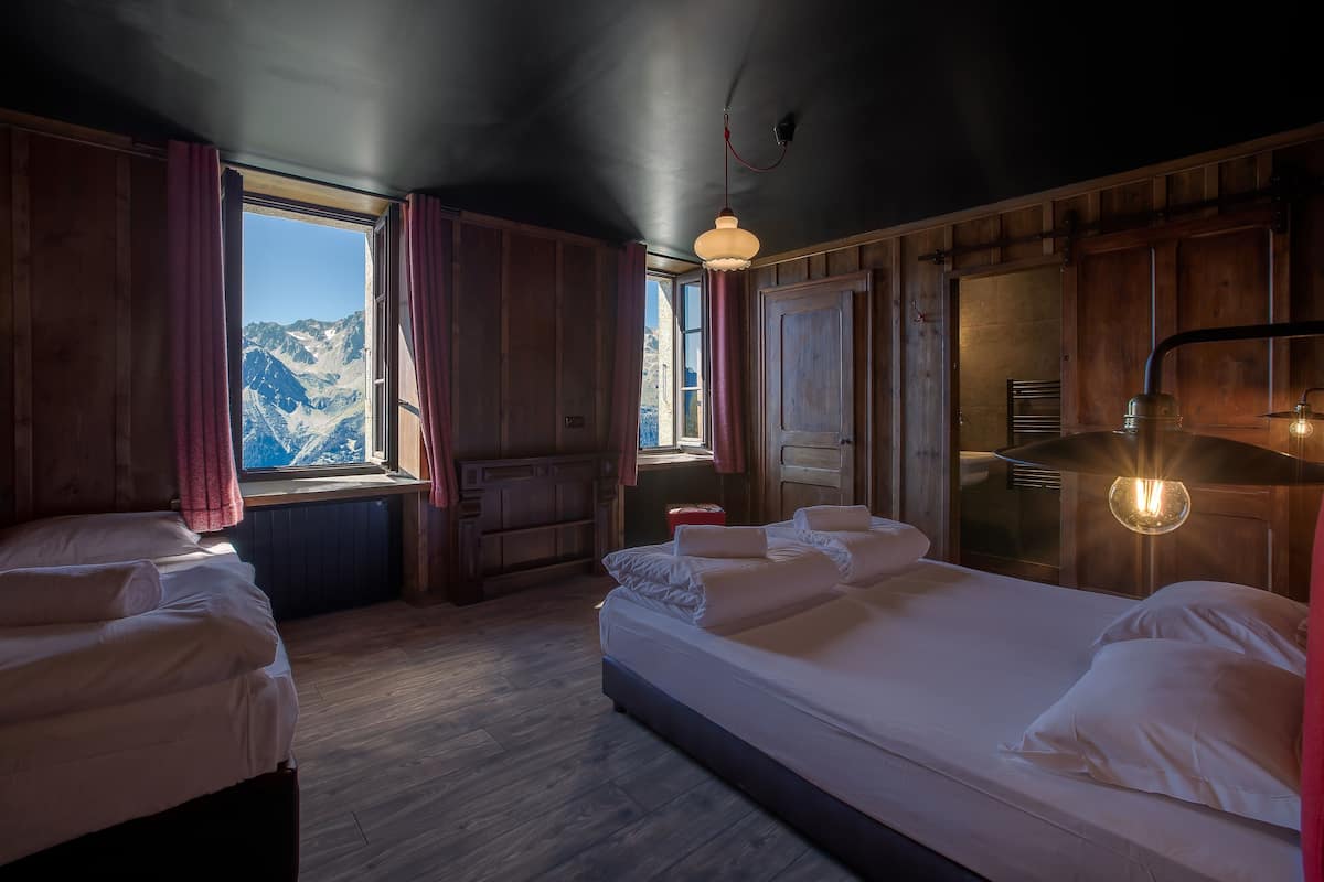 Une chambre avec deux lits, des murs en bois, une fenêtre donnant sur la montagne et un luminaire suspendu.