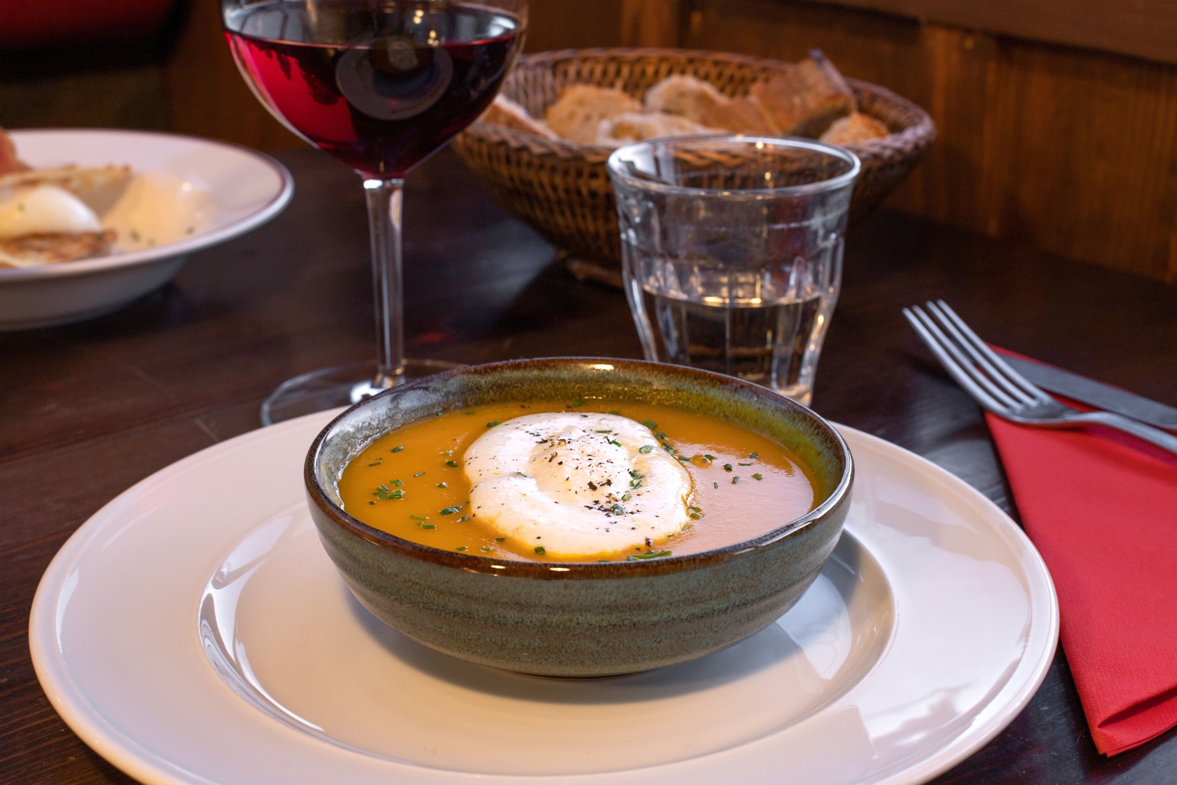A bowl of soup with a poached egg on top, accompanied by a glass of red wine and a glass of water on a table.