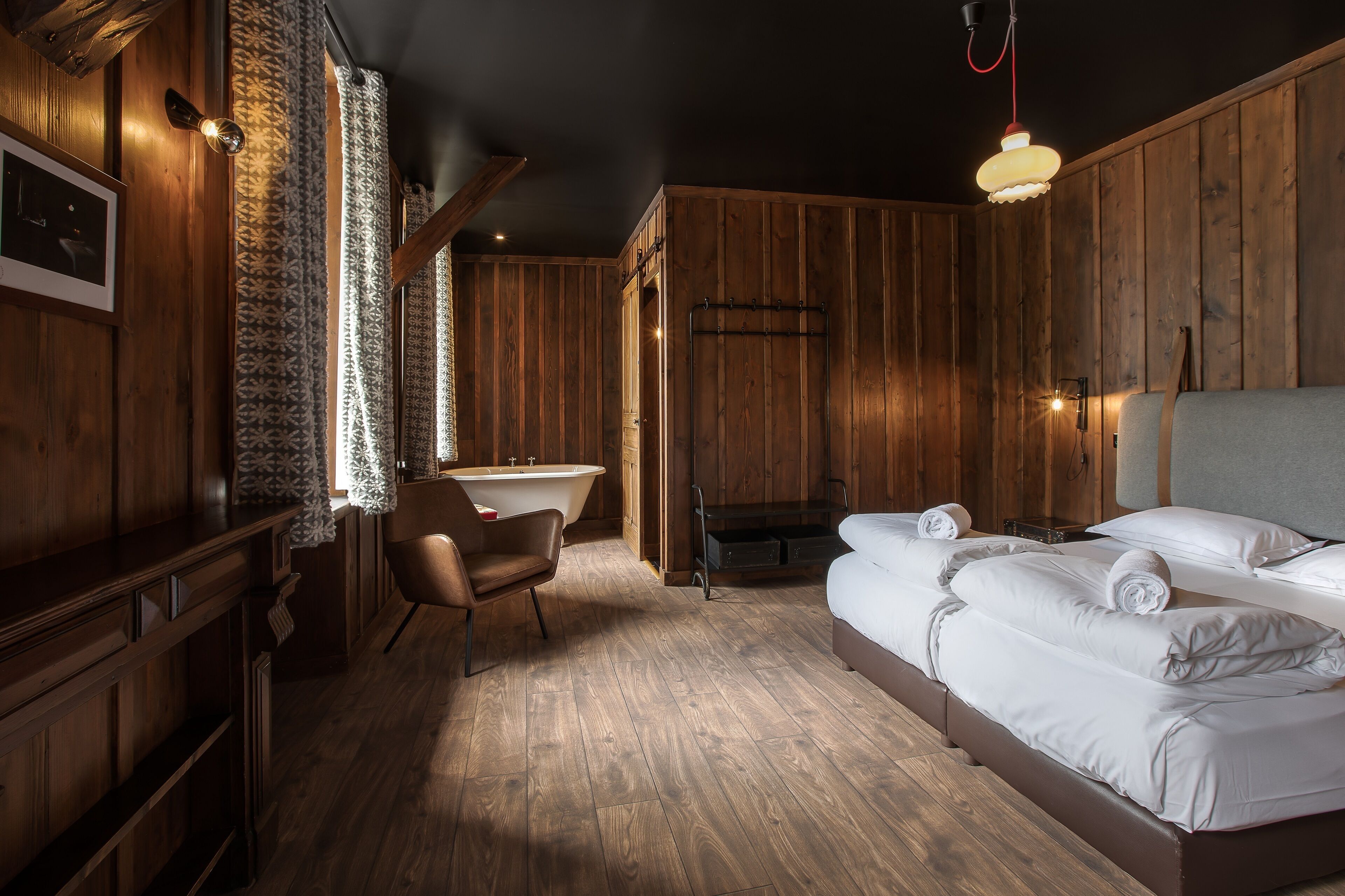 Una habitación con paneles de madera, con una cama, una silla, un lavamanos y una chimenea.