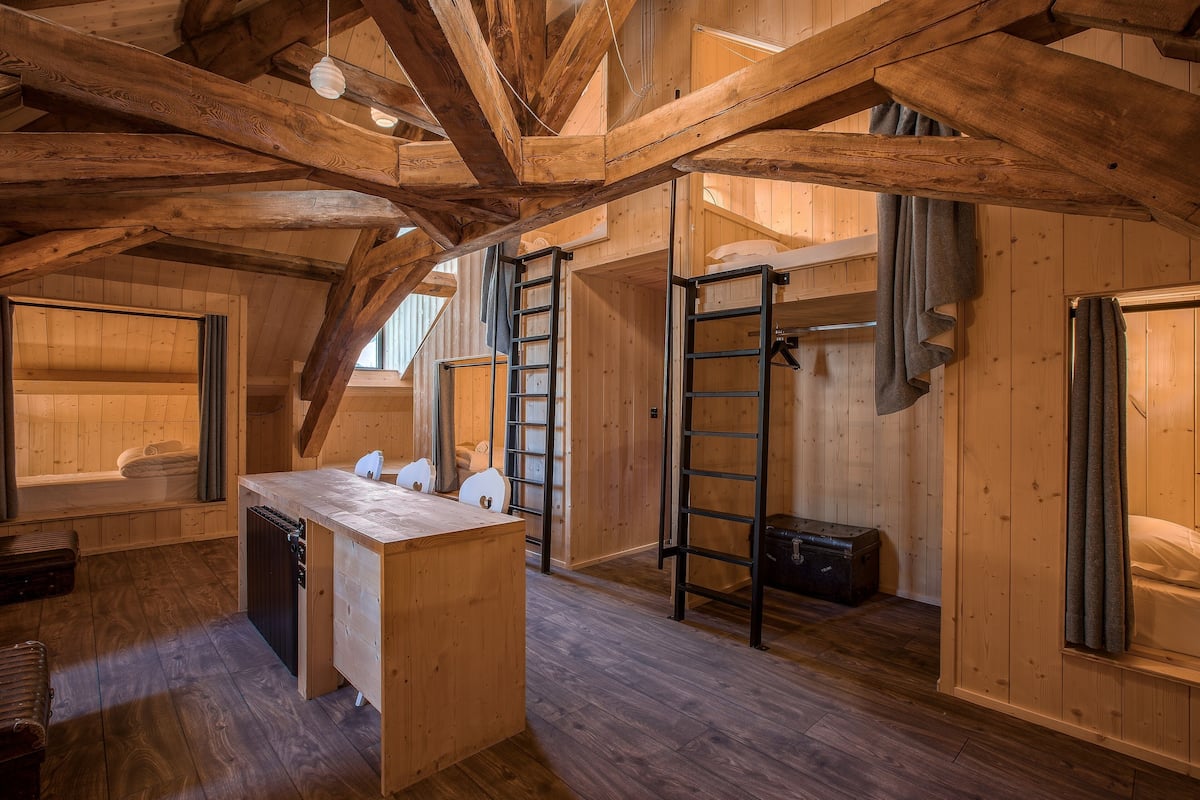 L’intérieur d’un chalet rustique en bois, avec un lit en mezzanine, une petite cuisine et un plafond en bois avec des poutres apparentes.