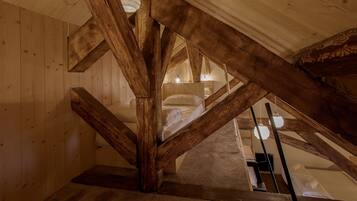 Un dormitorio de buhardilla con piso de madera, vigas a la vista, una cama y una lámpara colgante.
