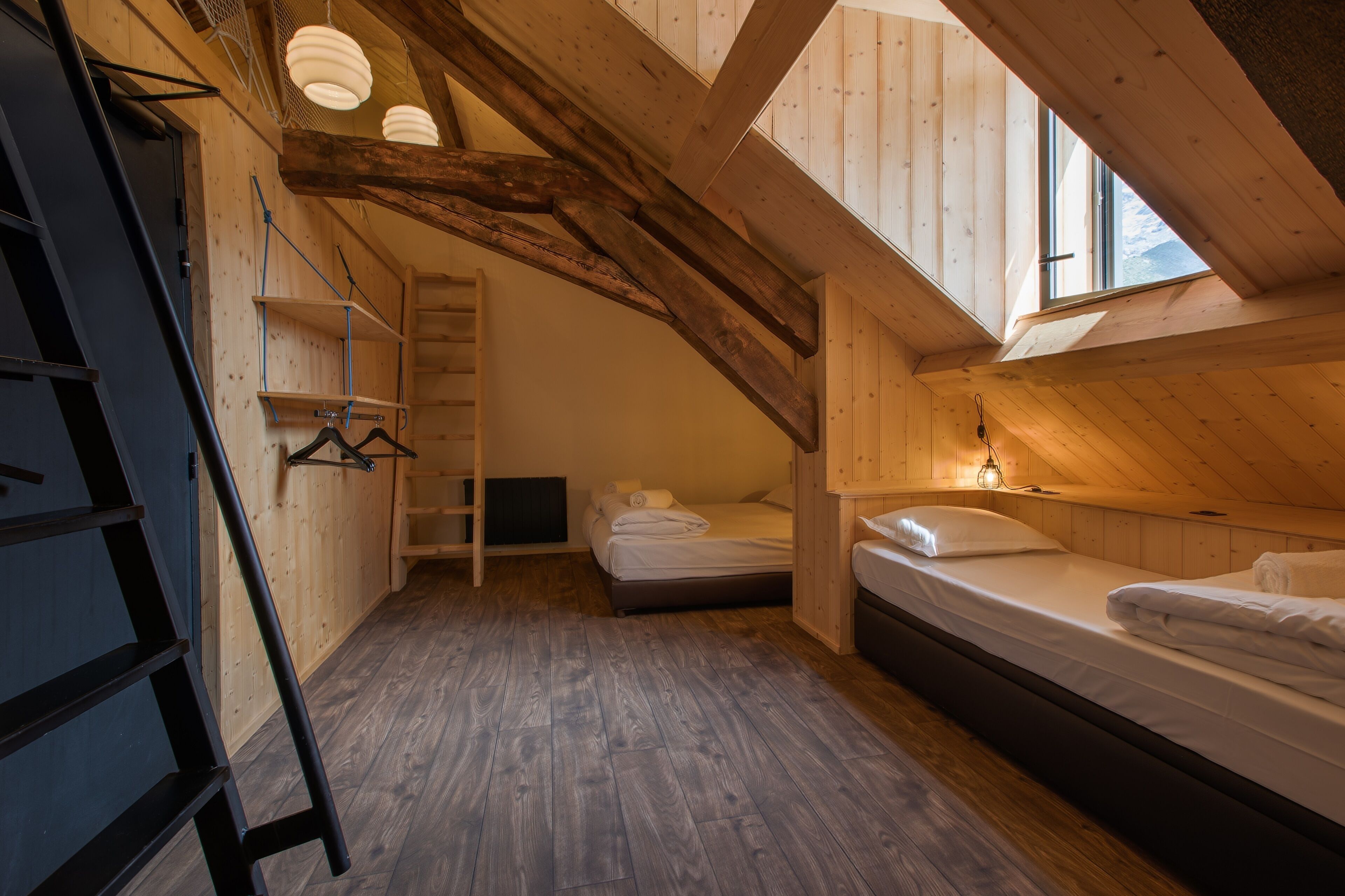 A cozy attic bedroom with wooden beams, a loft bed, a ladder, and a small window.