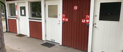 Une rangée de toilettes publiques mobiles, peintes en blanc et en rouge, avec une signalisation claire indiquant les différents équipements.