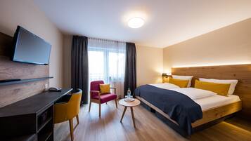 A modern hotel room with a bed, a desk, a chair, and a television.