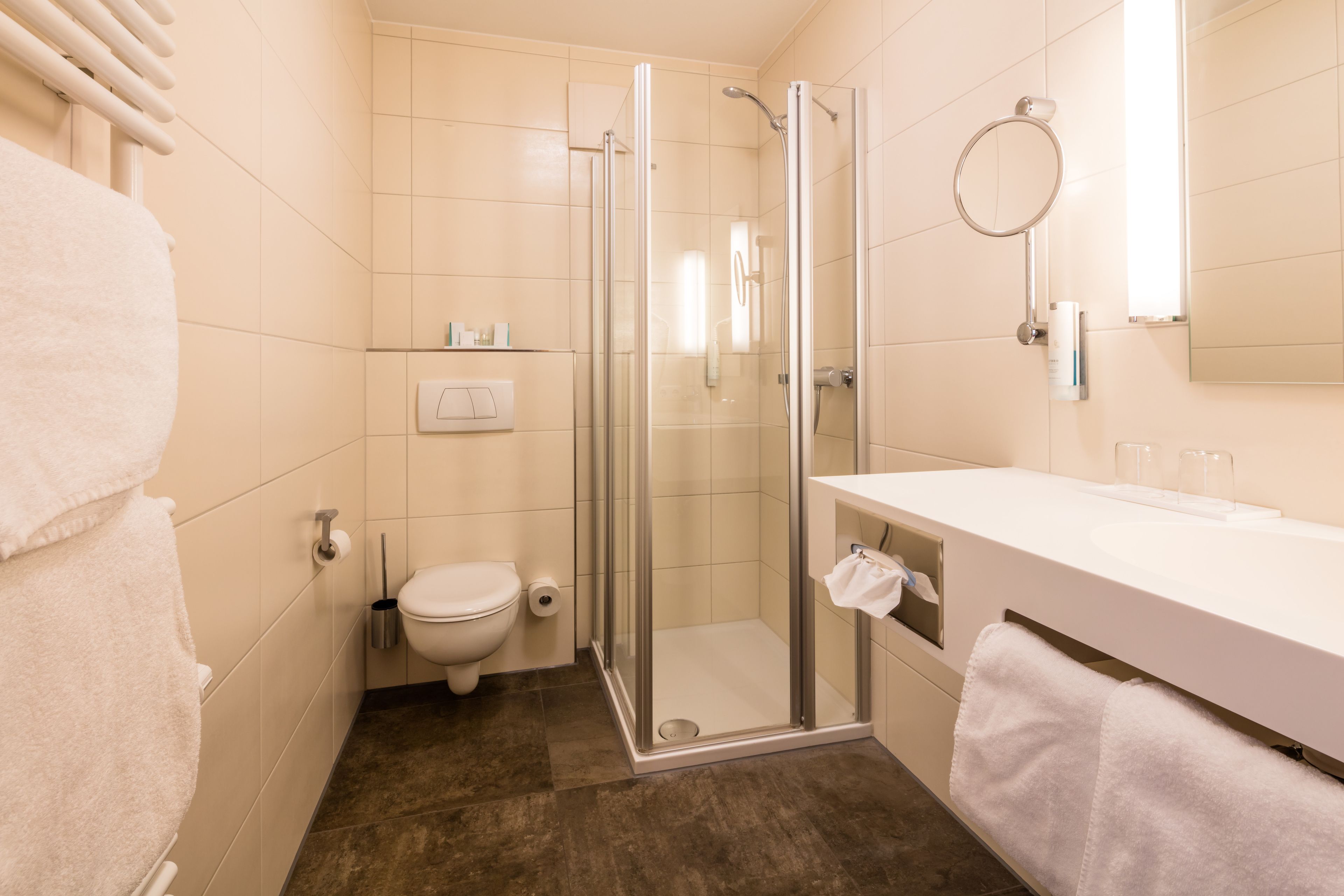 A modern bathroom with a glass-enclosed shower, a toilet, and a white sink with a towel hanging on the side.