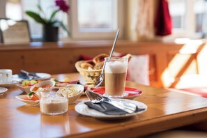 A dining table with various dishes, including a glass of milk, a bowl of fruit, and a basket of bread. - Landhotel Endhart (Landsberg am Lech)