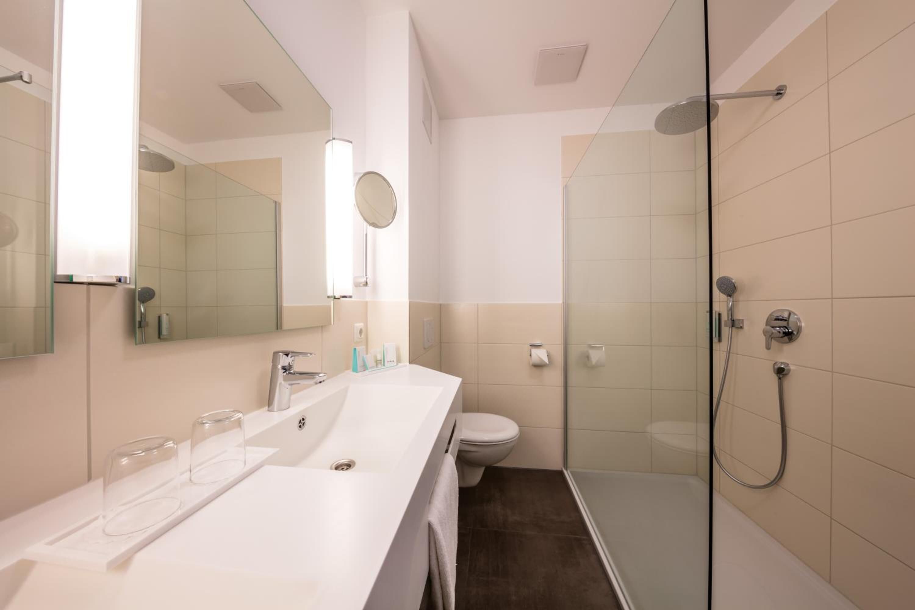 A modern bathroom with a glass-enclosed shower, a white sink with a mirror, and a toilet.