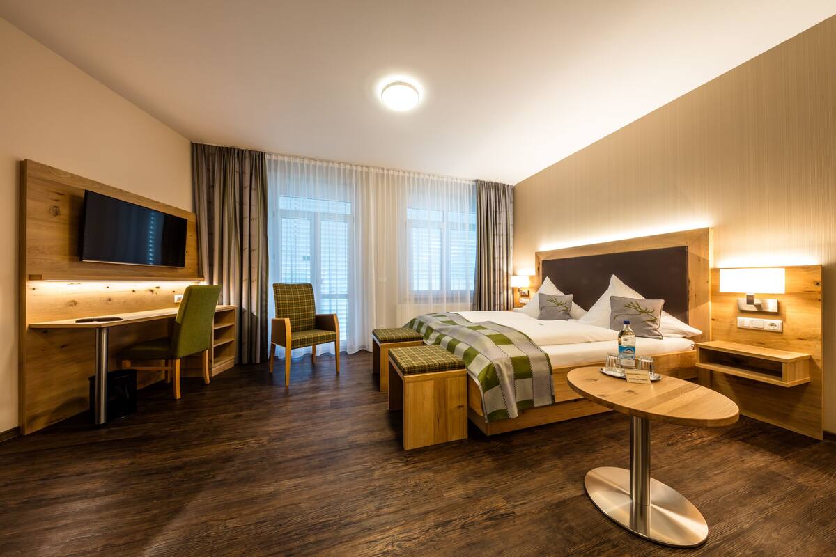 Una habitación de hotel moderna con cama, escritorio, silla y televisor montado en la pared.