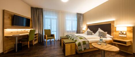 A modern hotel room with a bed, desk, chair, and a TV mounted on the wall.