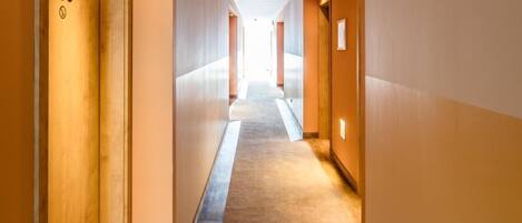 Corredor de hotel com piso de madeira, paredes bege e portas numeradas 103.
