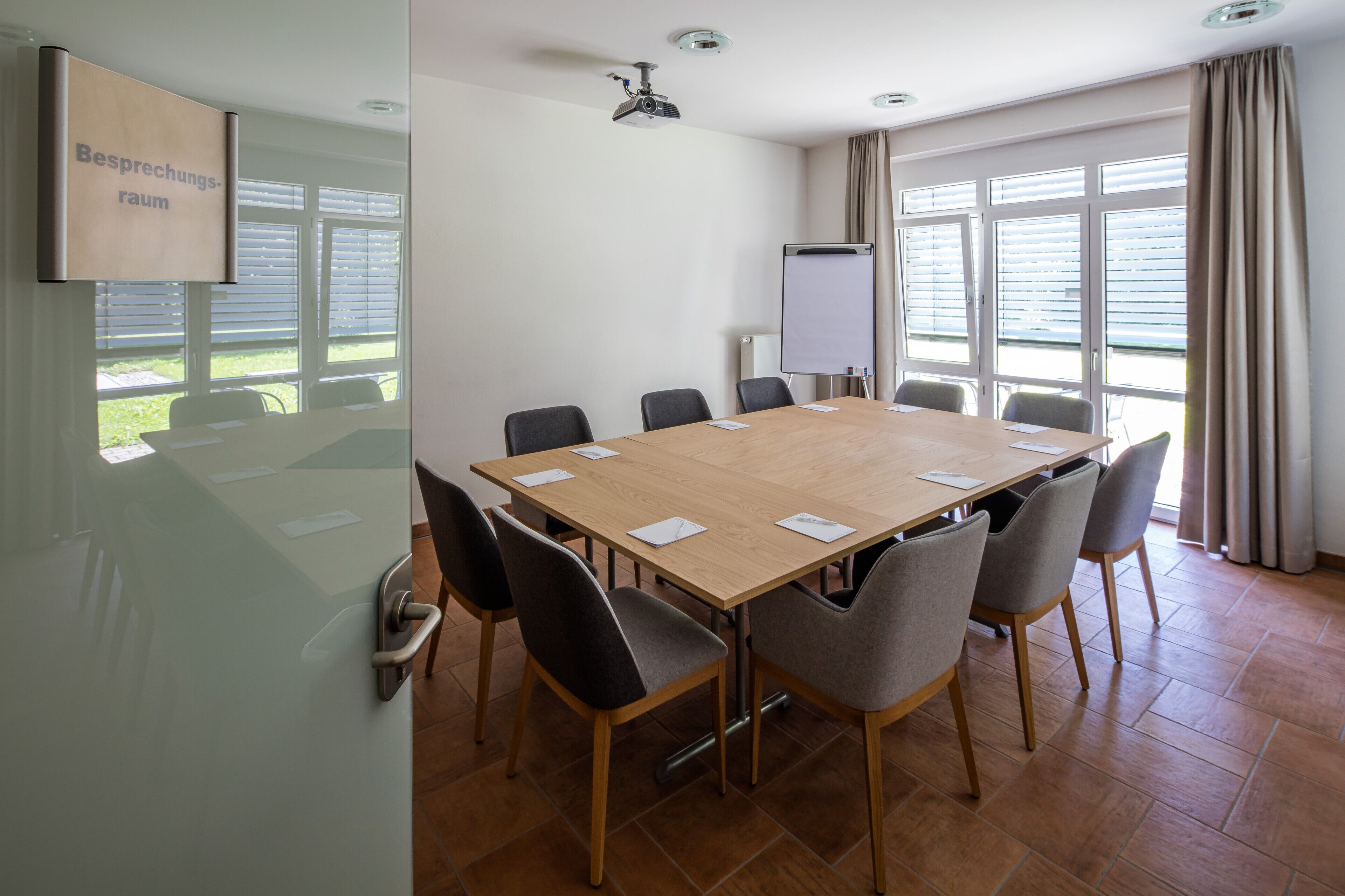 Ein Konferenzraum mit langem Tisch, Stühlen, einem Projektor und einer Whiteboard-Tafel.