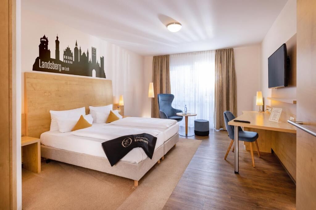 Ein Hotelzimmer mit Bett, Schreibtisch, Stuhl, Fernseher und einer Wanddekoration mit Stadtansicht.
