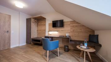 Ein modernes Schlafzimmer im Loft-Stil mit schrägverdeckter Decke, Holzboden, einem eingebauten Schreibtisch mit Flachbildfernseher, einem blauen Stuhl mit Muster, einem kleinen runden Tisch mit Glas und einer Wasserflasche.