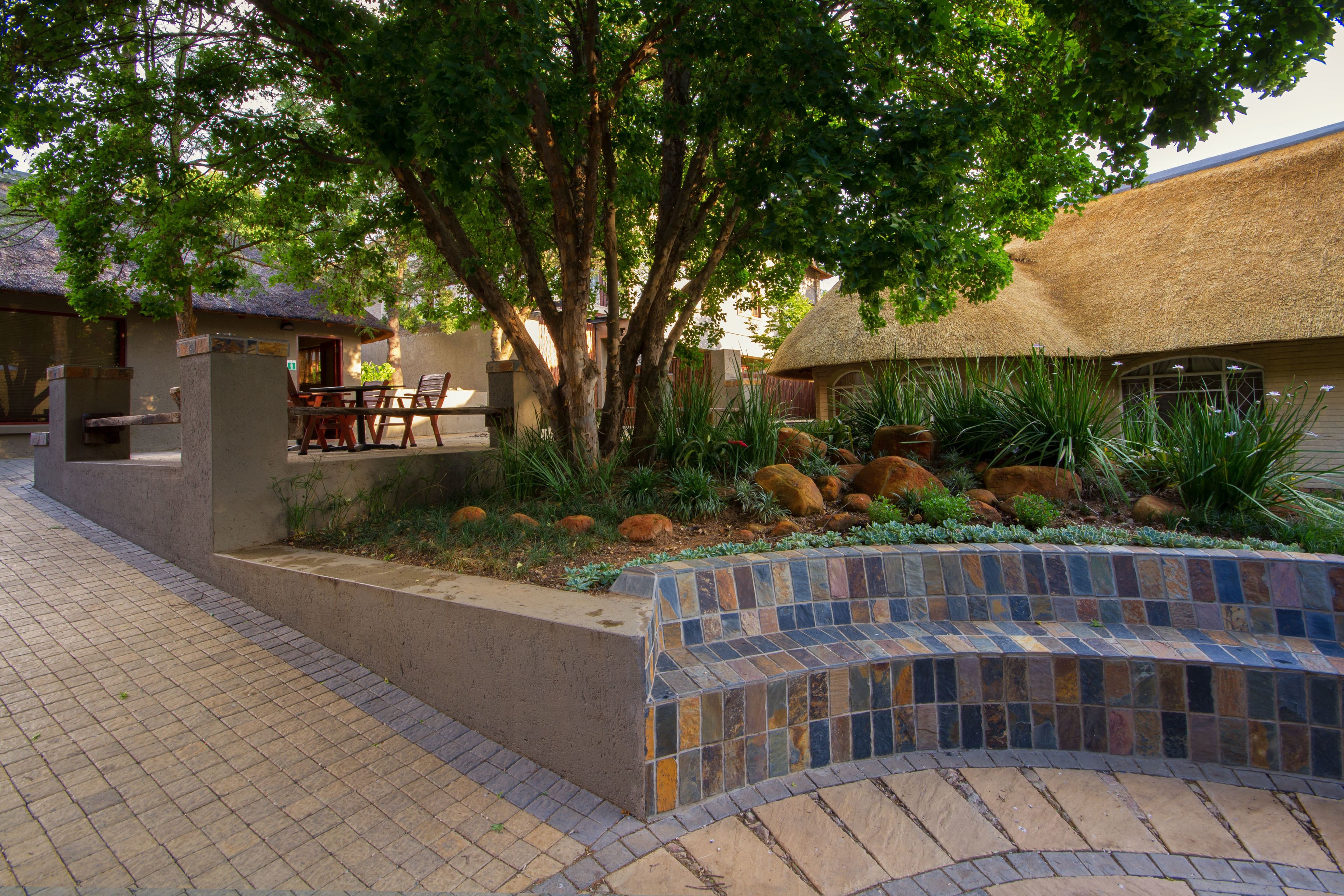 A courtyard with a tiled bench, a thatched-roof building, and a dining area with outdoor furniture.