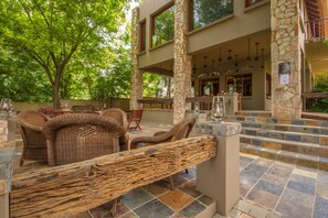 An outdoor patio with wicker furniture, stone pillars, and a stone staircase leading to an upper level. - Africlassic River Lodge- Rivonia (Sandton)
