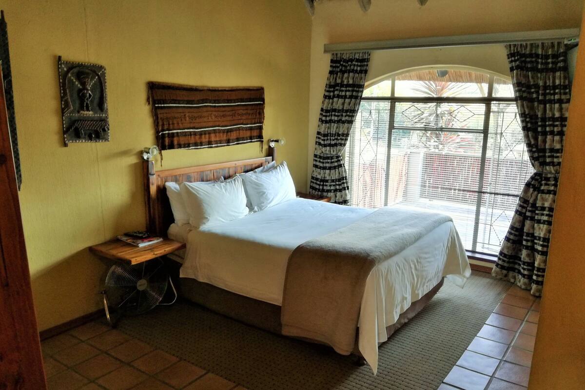 A neatly made bed with white linens, a wooden headboard, and a small bedside table with a fan.