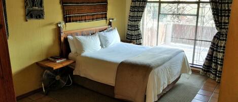 A neatly made bed with white linens, a wooden headboard, and a small bedside table with a fan.