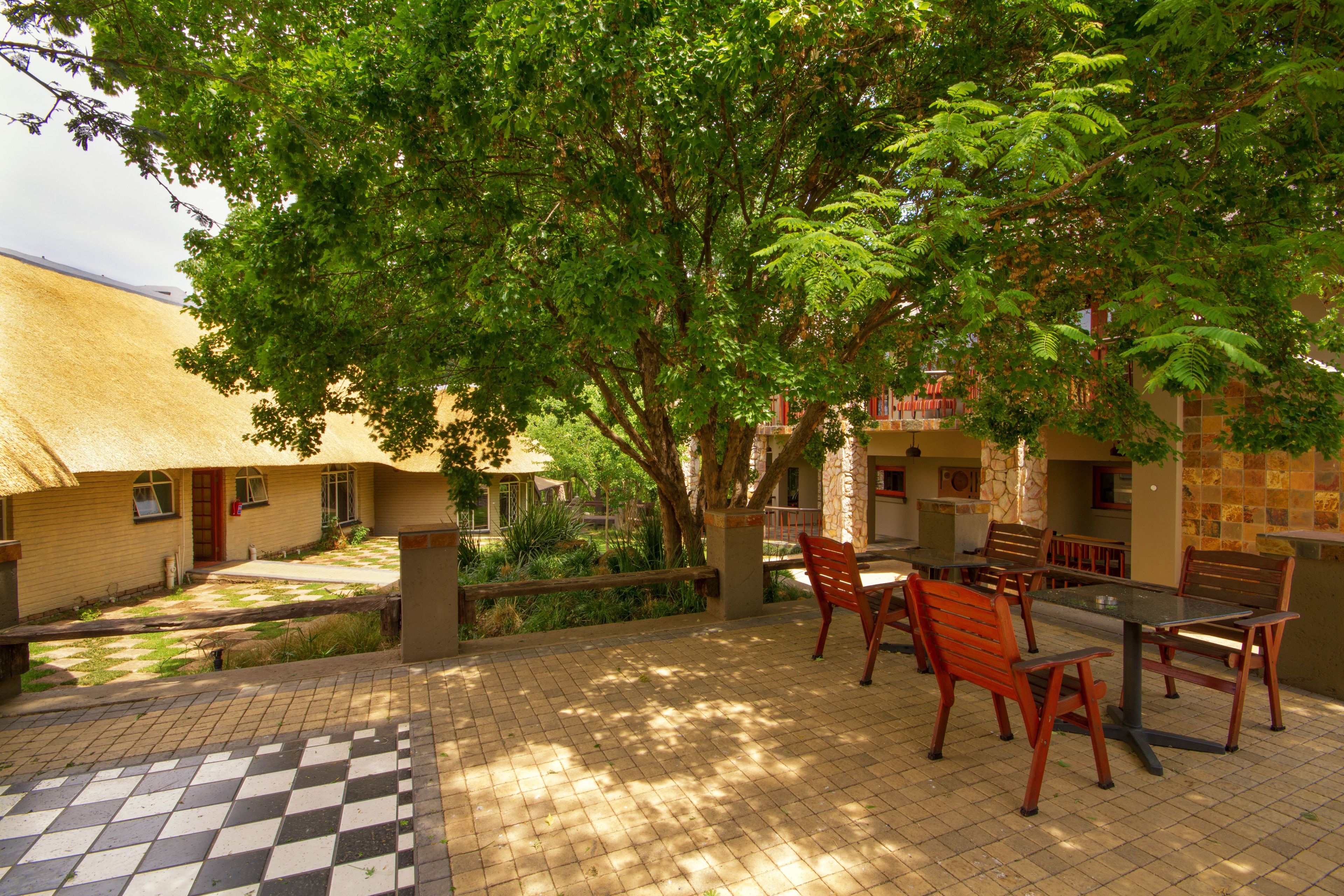 A patio with a checkered floor, wooden furniture, and a thatched-roof building.