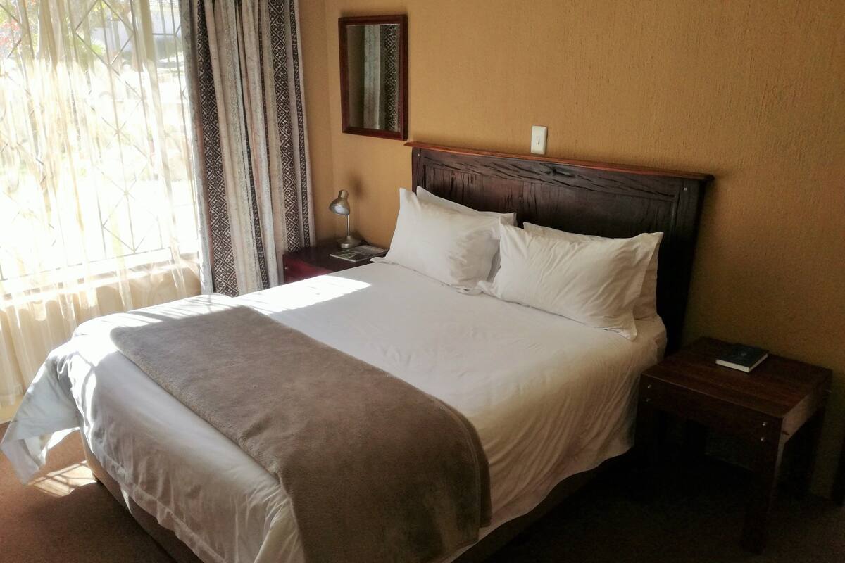 A neatly made bed with a headboard, a bedside table with a lamp, and a mirror on the wall.