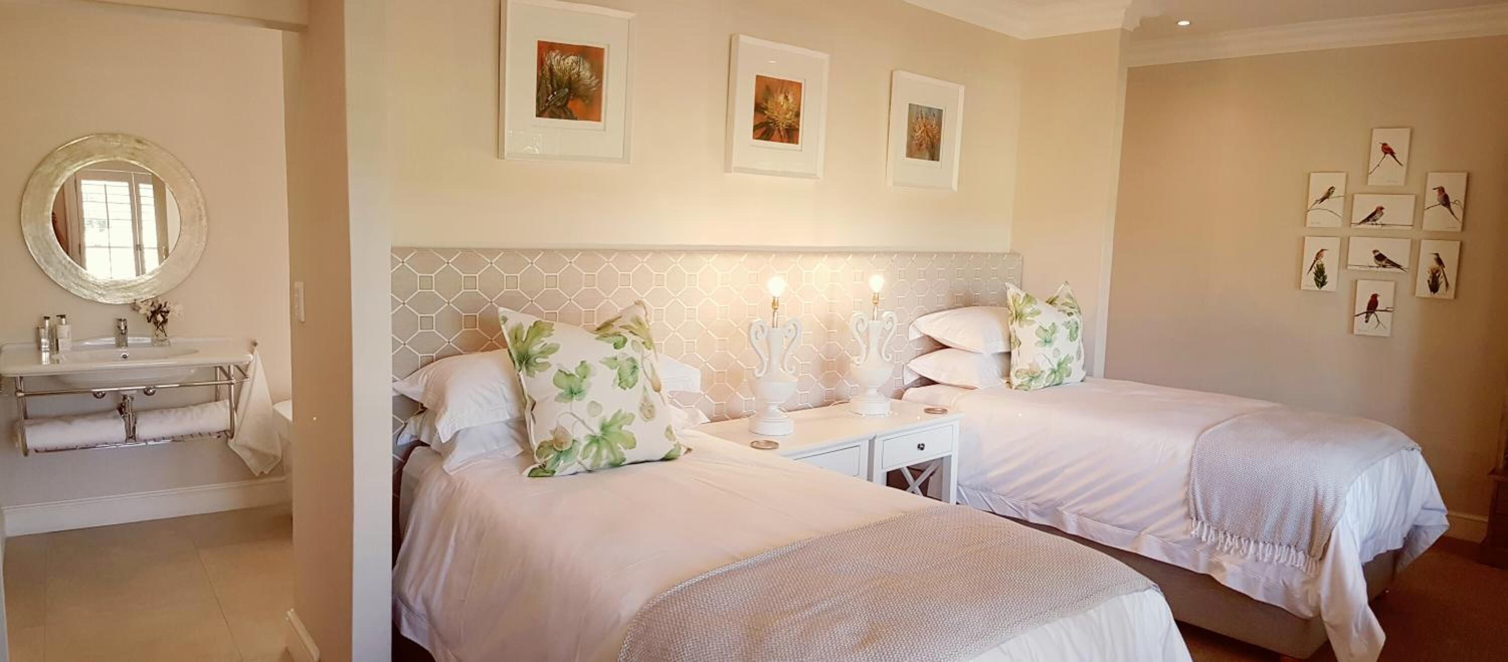A hotel room with two beds, a nightstand, a mirror, and a bathroom with a sink and towel rack.