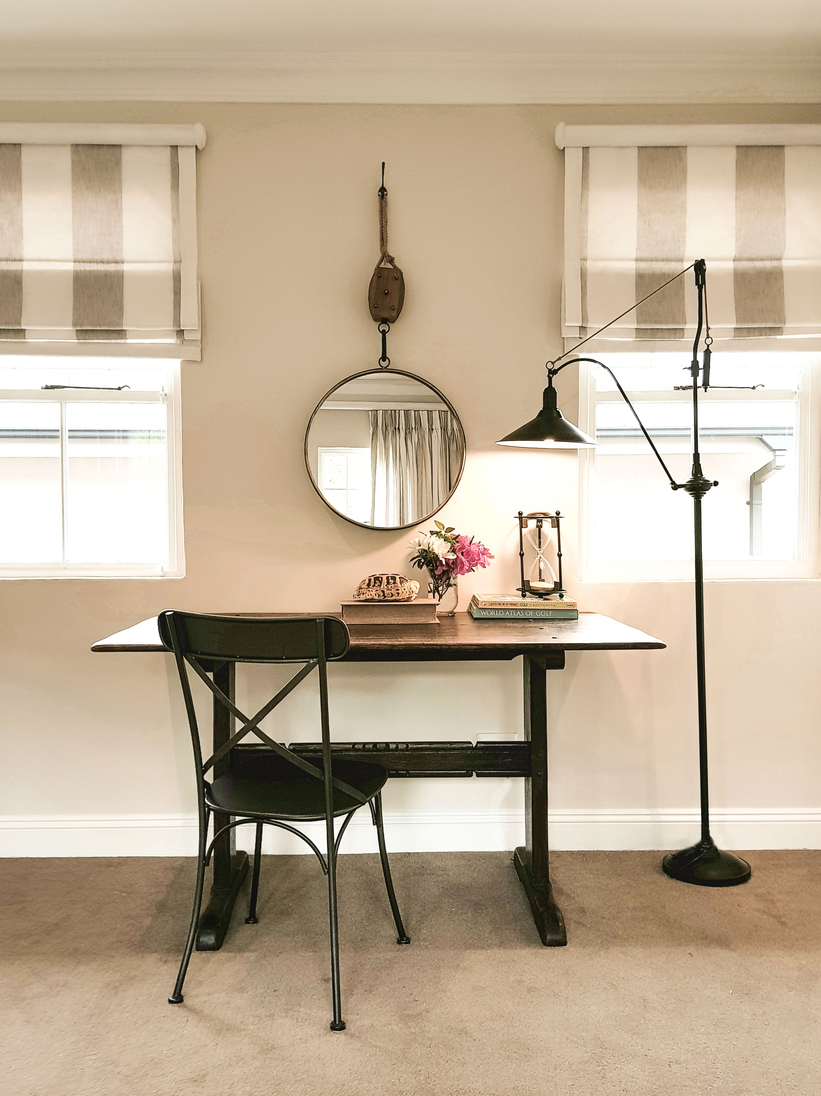 A room with a desk, chair, lamp, and a round mirror on the wall.