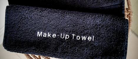 Una toalla negra con bordados que dicen "Golf Shoes" y "Make-Up Towel", colgada de una silla de mimbre.