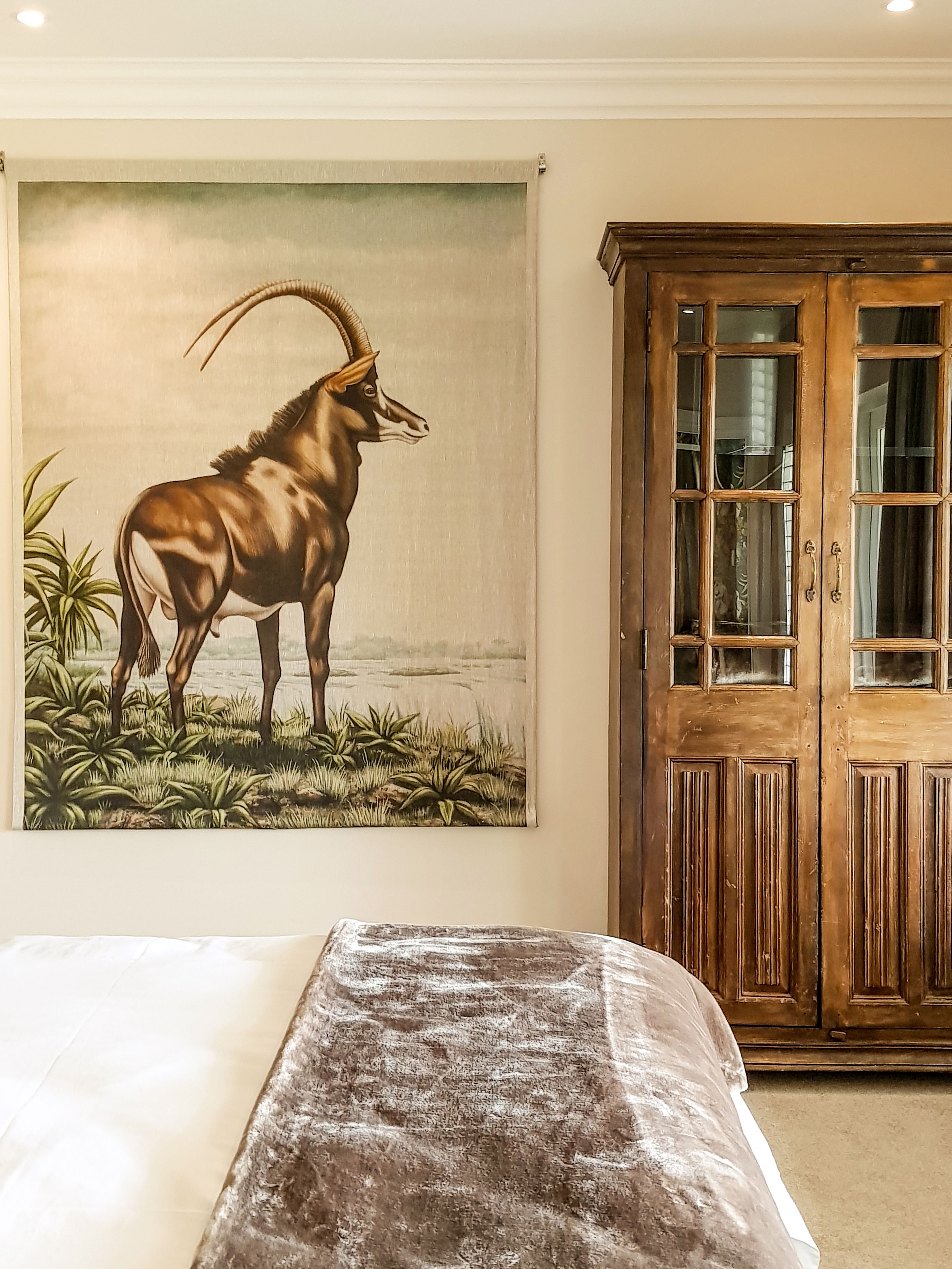 A bedroom with a bed, a large painting of an animal, and a wooden cabinet.