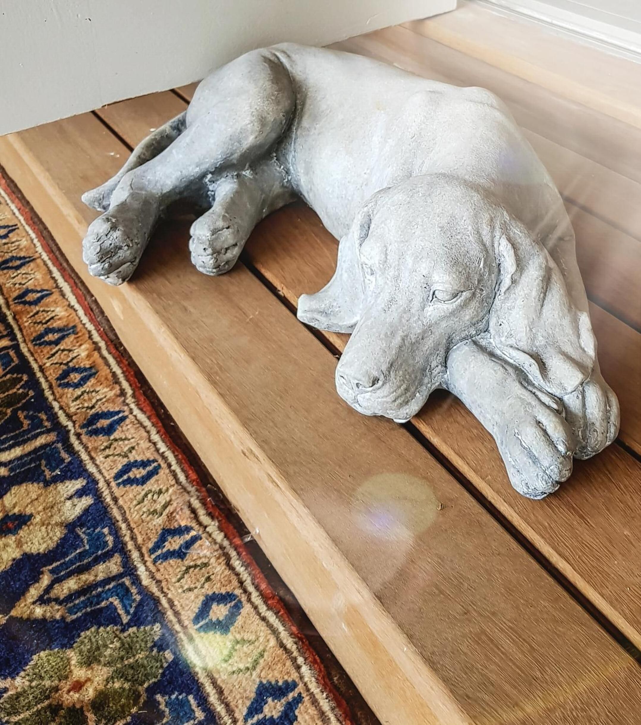 Een stenen beeldhouwwerk van een rustende hond op een houten bank.