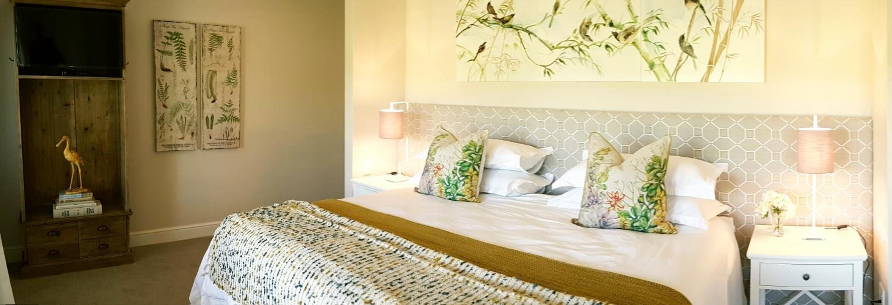 Quarto bem organizado com cama, duas mesas de cabeceira, um criado-mudo, um abajur e um quadro na parede.