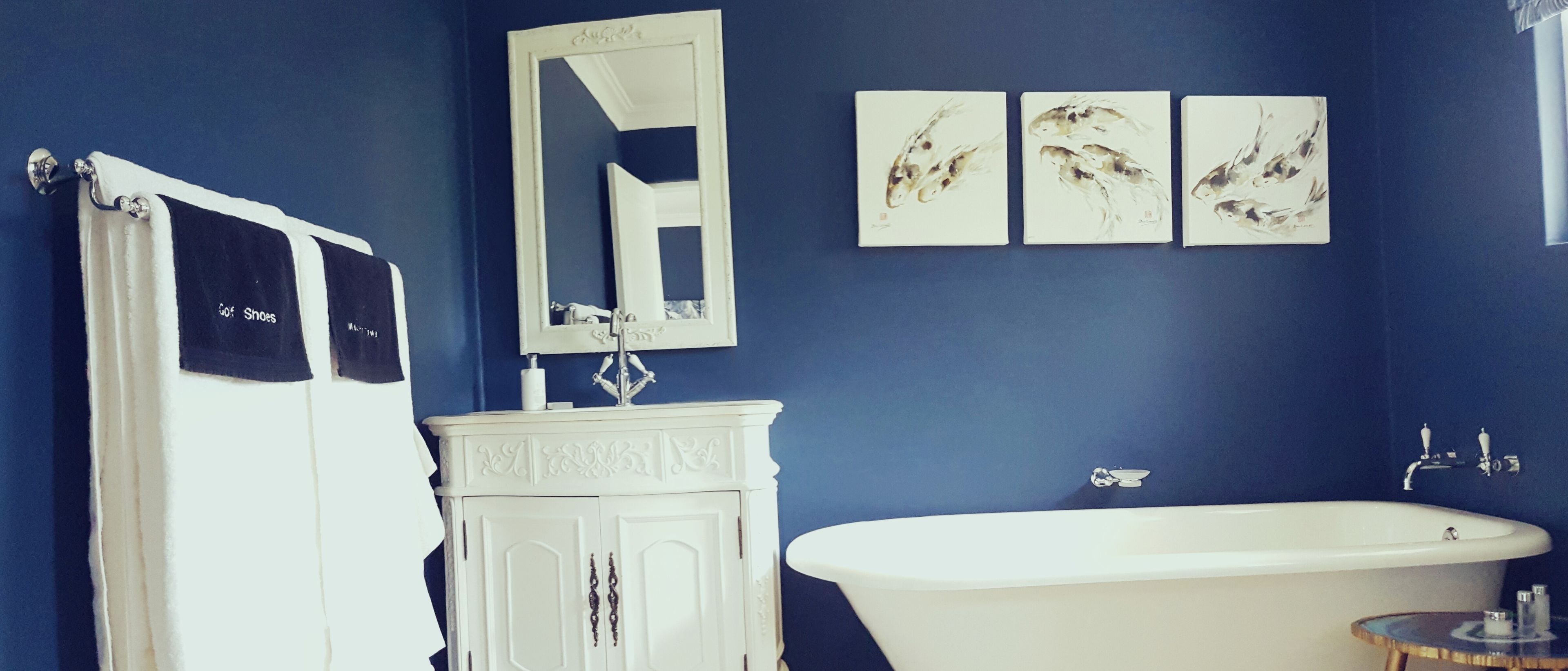 A bathroom with a white bathtub, a white vanity with a mirror, and three wall-mounted paintings.