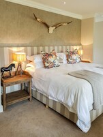 Un dormitorio con una cama grande, cabecera a rayas, almohadones decorativos, una mesita de noche de madera con una figurita de caballo y un atornillo en la pared.