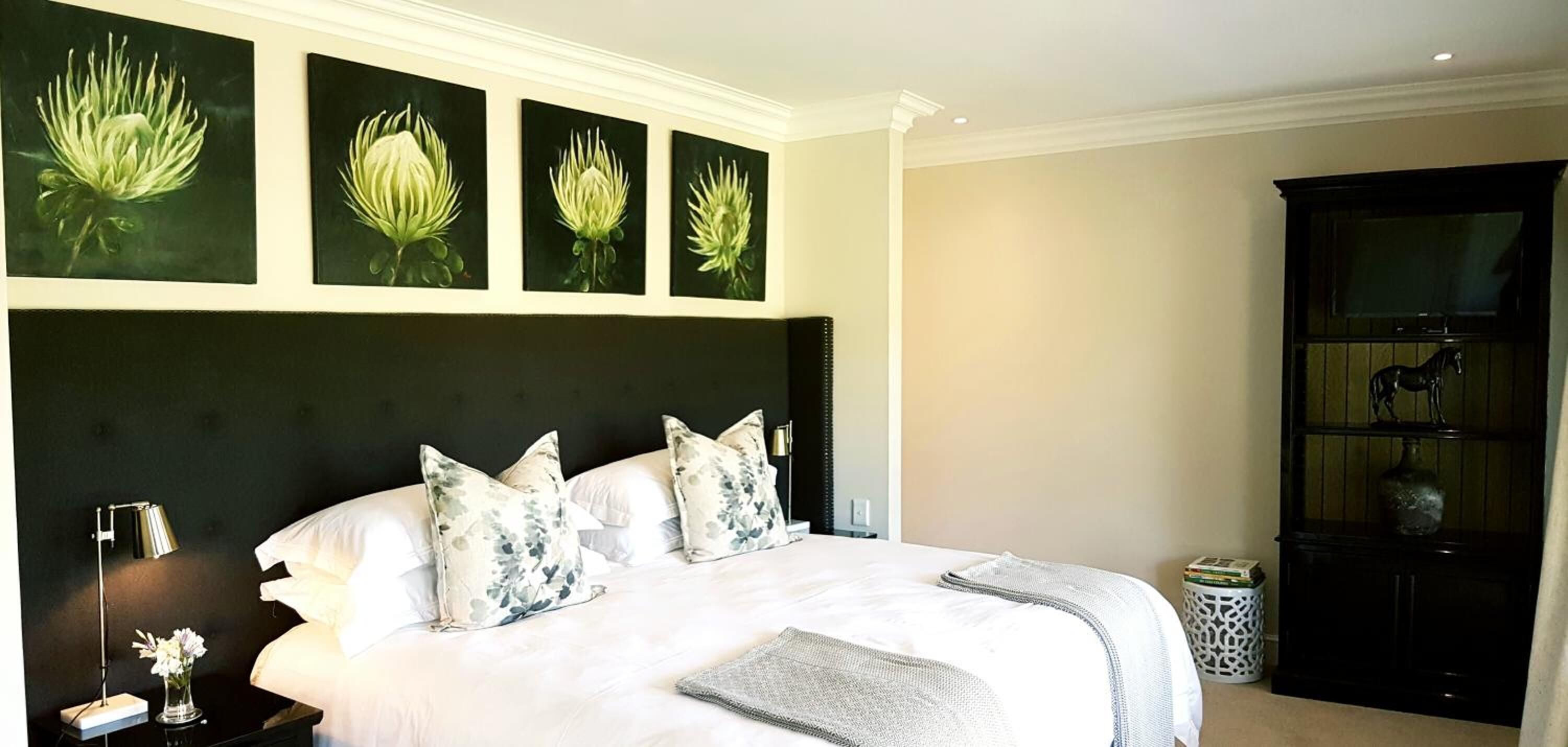 Una habitación de hotel con una cama grande, decoración floral en la pared, una mesita de noche con lámpara y una estantería.