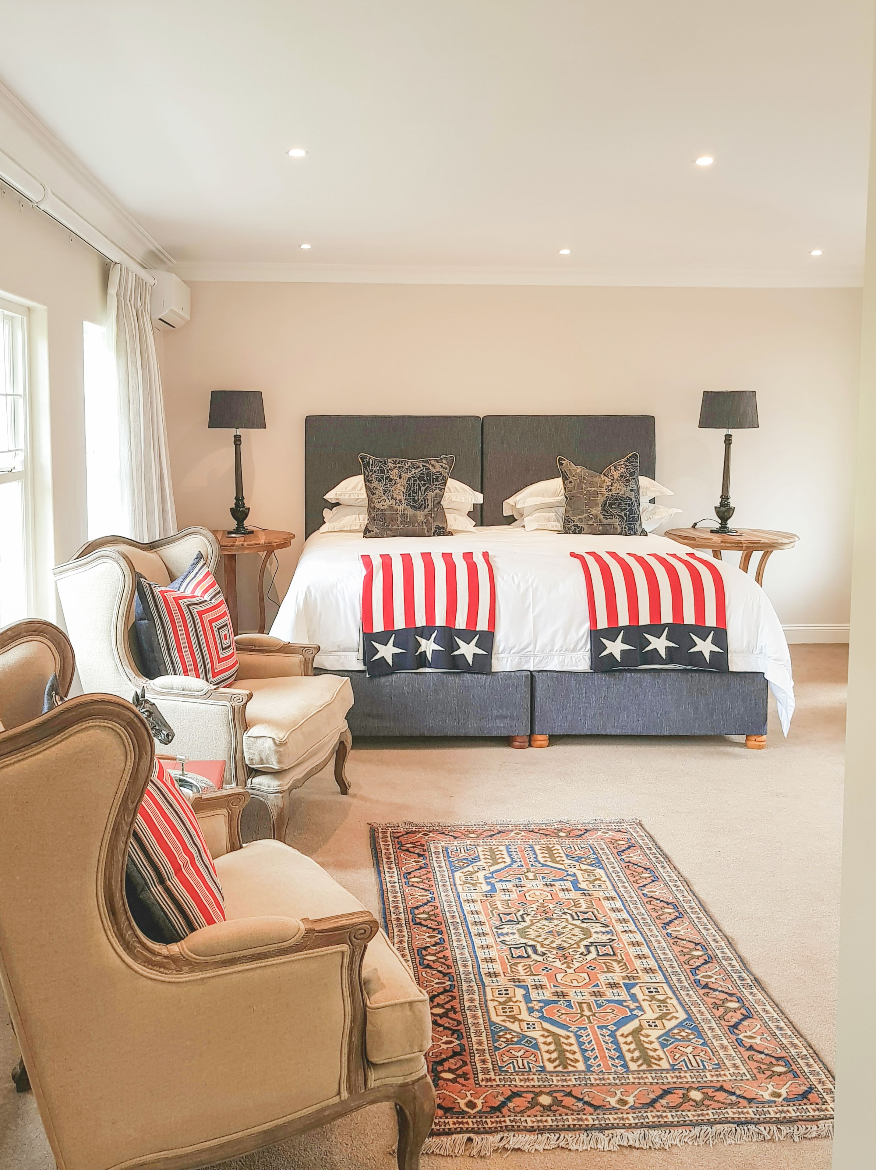 A bedroom with a large bed, two bedside tables with lamps, a chair, and a patterned rug.