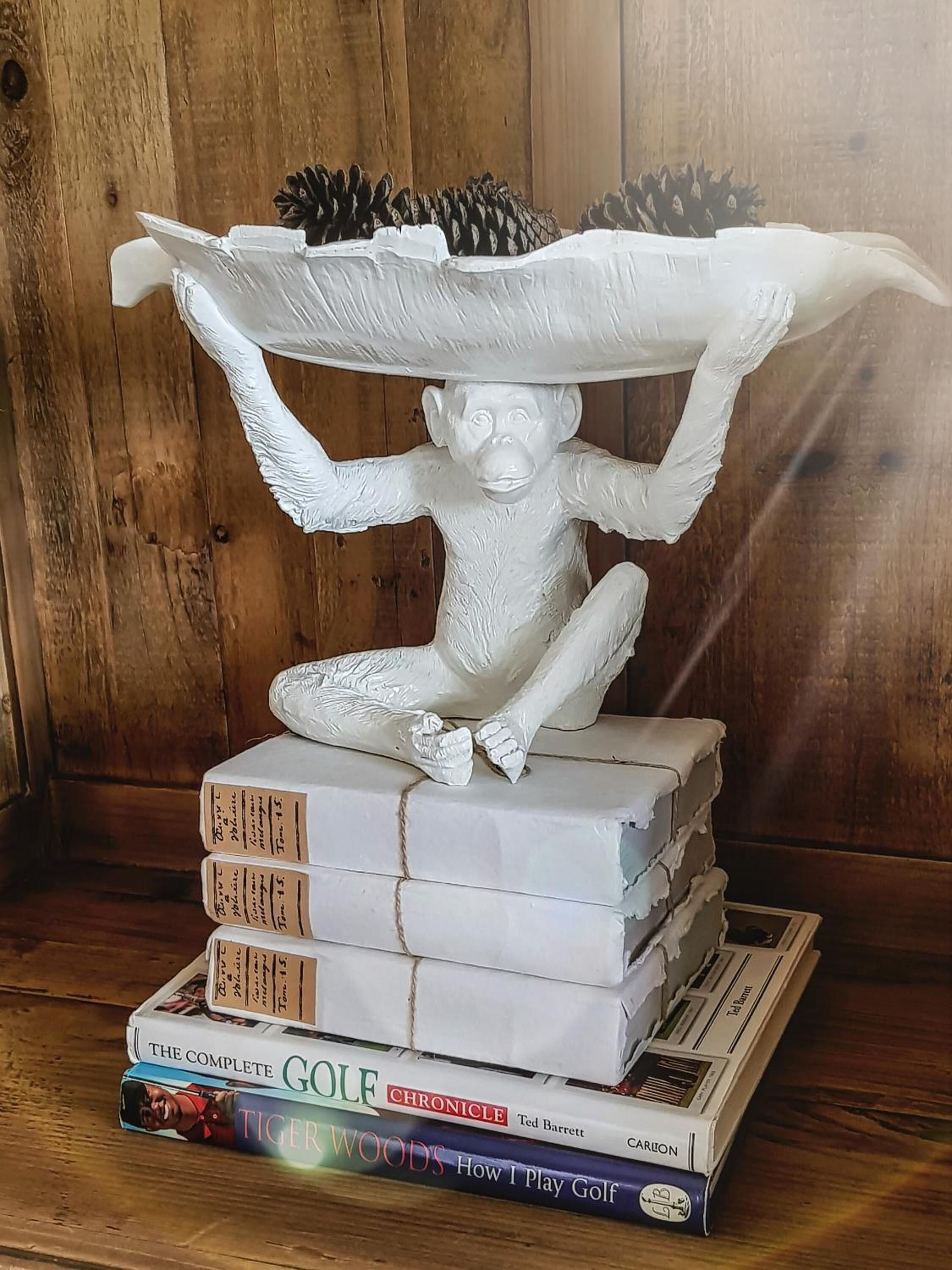 A sculpture of a monkey balancing a large bowl on its head, placed on top of a stack of books.
