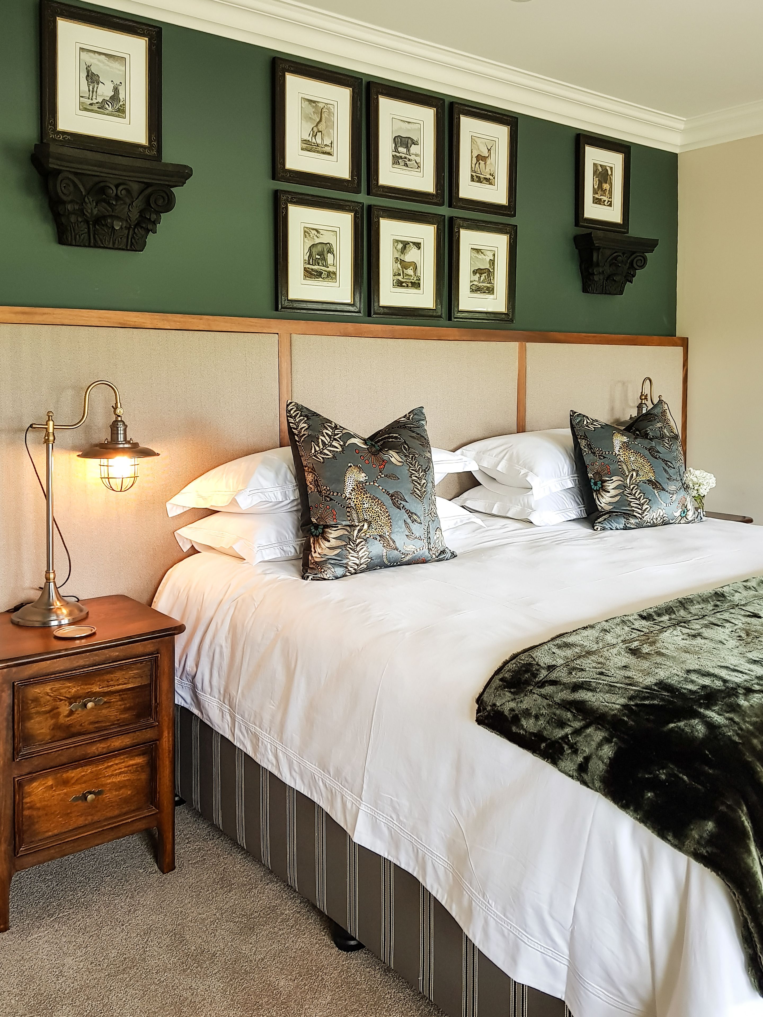 A neatly arranged bedroom with a large bed, a bedside table with a lamp, and a series of framed pictures on the wall.