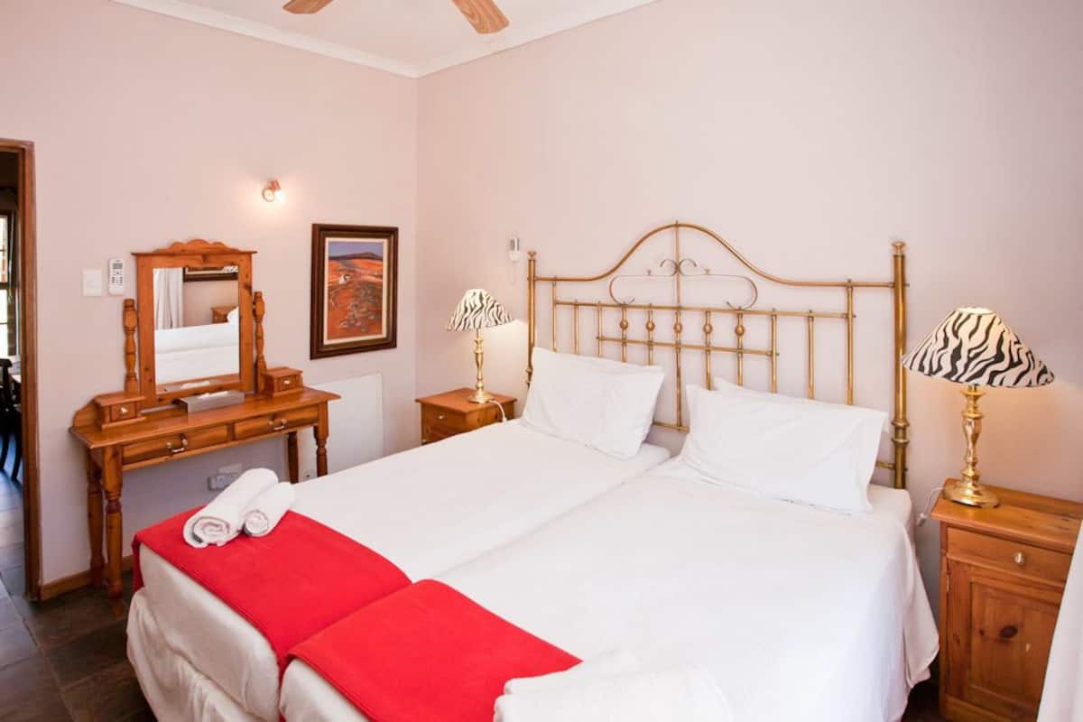 A hotel room with a large bed, a wooden dresser, a mirror, two bedside lamps, and a red blanket on the bed.
