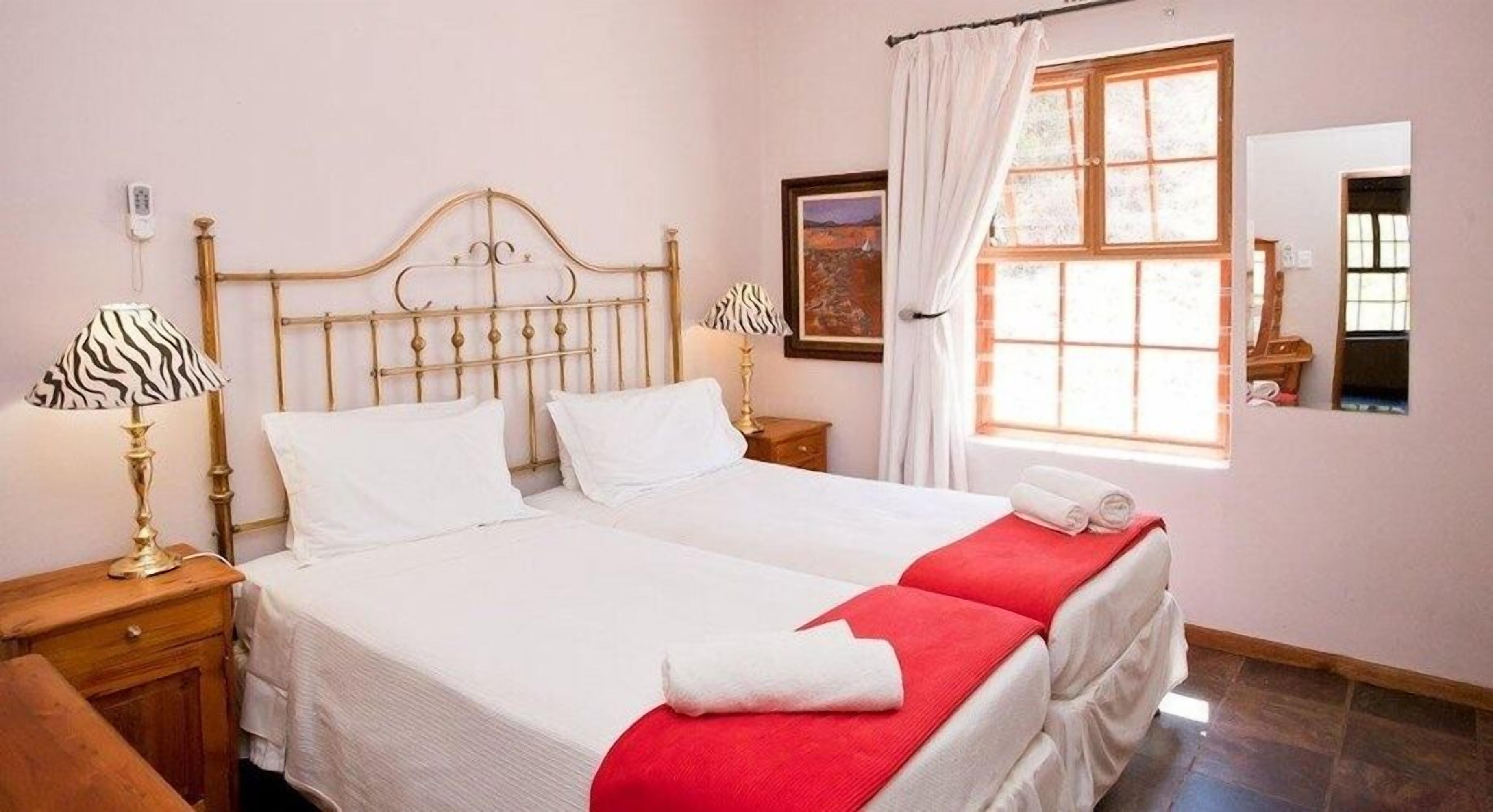 Un letto matrimoniale con biancheria da letto bianca e coperte rosse, un comodino con una lampada e una finestra con tende.