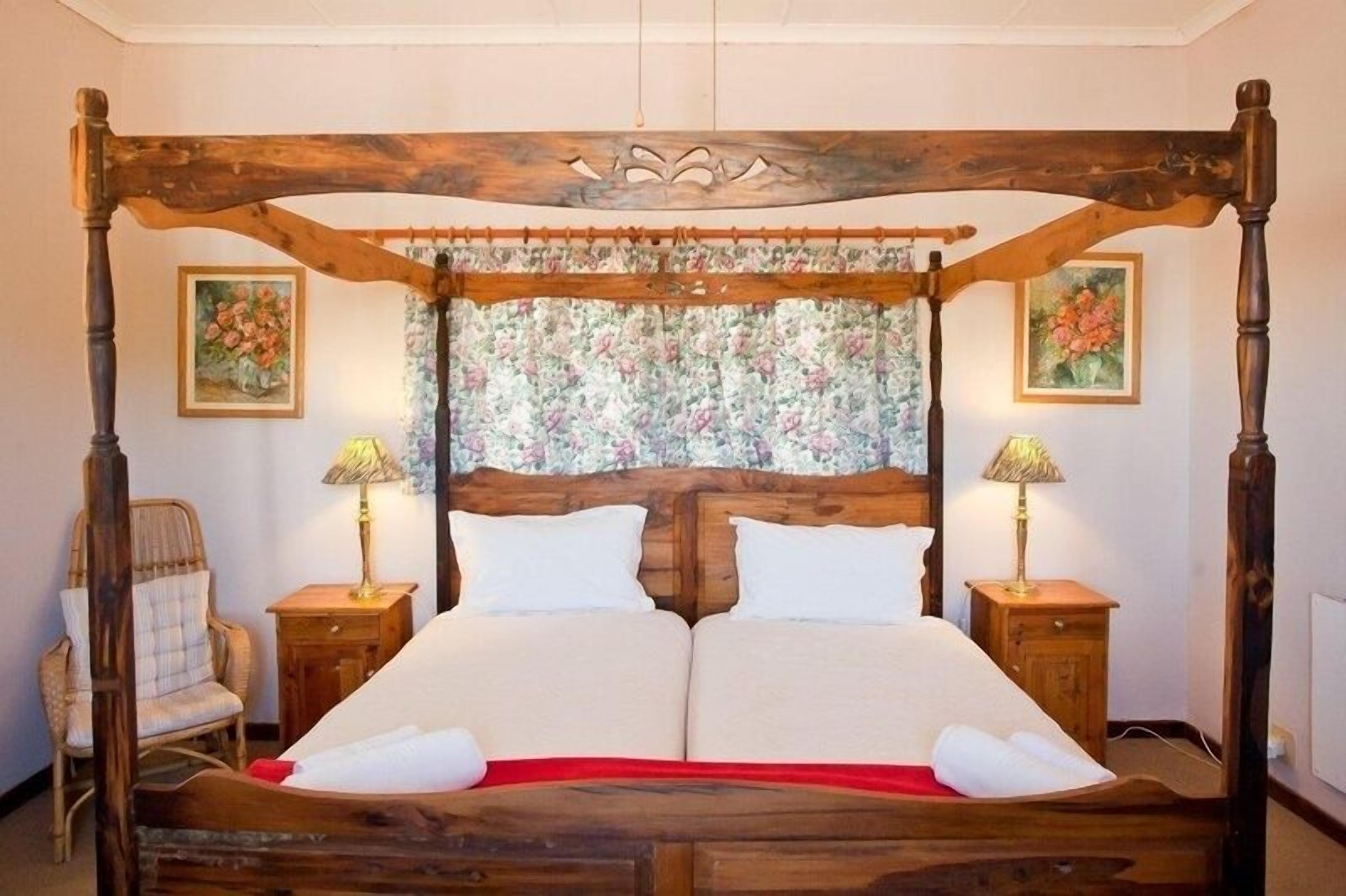 A four-poster bed with a floral headboard, two bedside tables with lamps, and a chair.