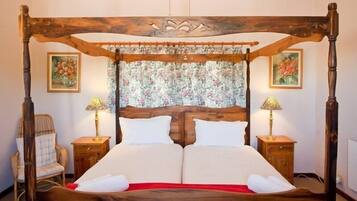 A four-poster bed with a floral headboard, two bedside tables with lamps, and a chair.