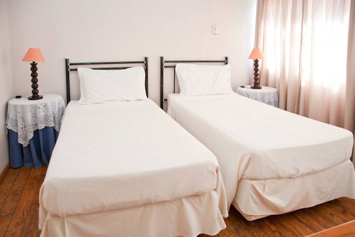 Two single beds with white bedding, a wooden floor, and a window with curtains.
