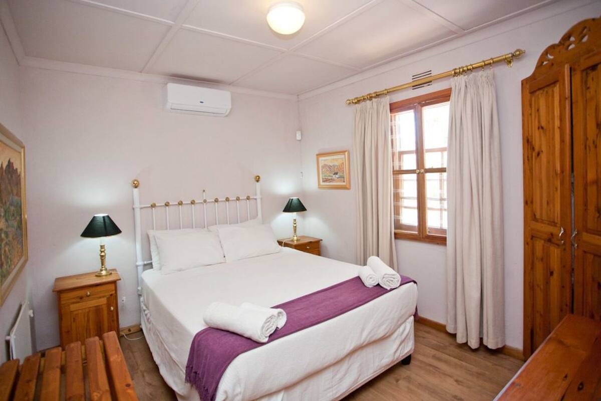 A neatly arranged bedroom with a large bed, two bedside tables with lamps, a wooden bench, a window with curtains, and a wooden wardrobe.