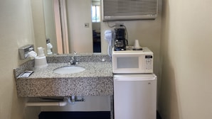 A bathroom with a sink, mirror, air conditioning unit, and a microwave. - Econo Lodge Las Vegas NM (Las Vegas)