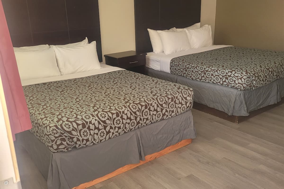 Une chambre d’hôtel comprenant deux lits simples avec des têtes de lit, une table de chevet et un luminaire fixé au mur.