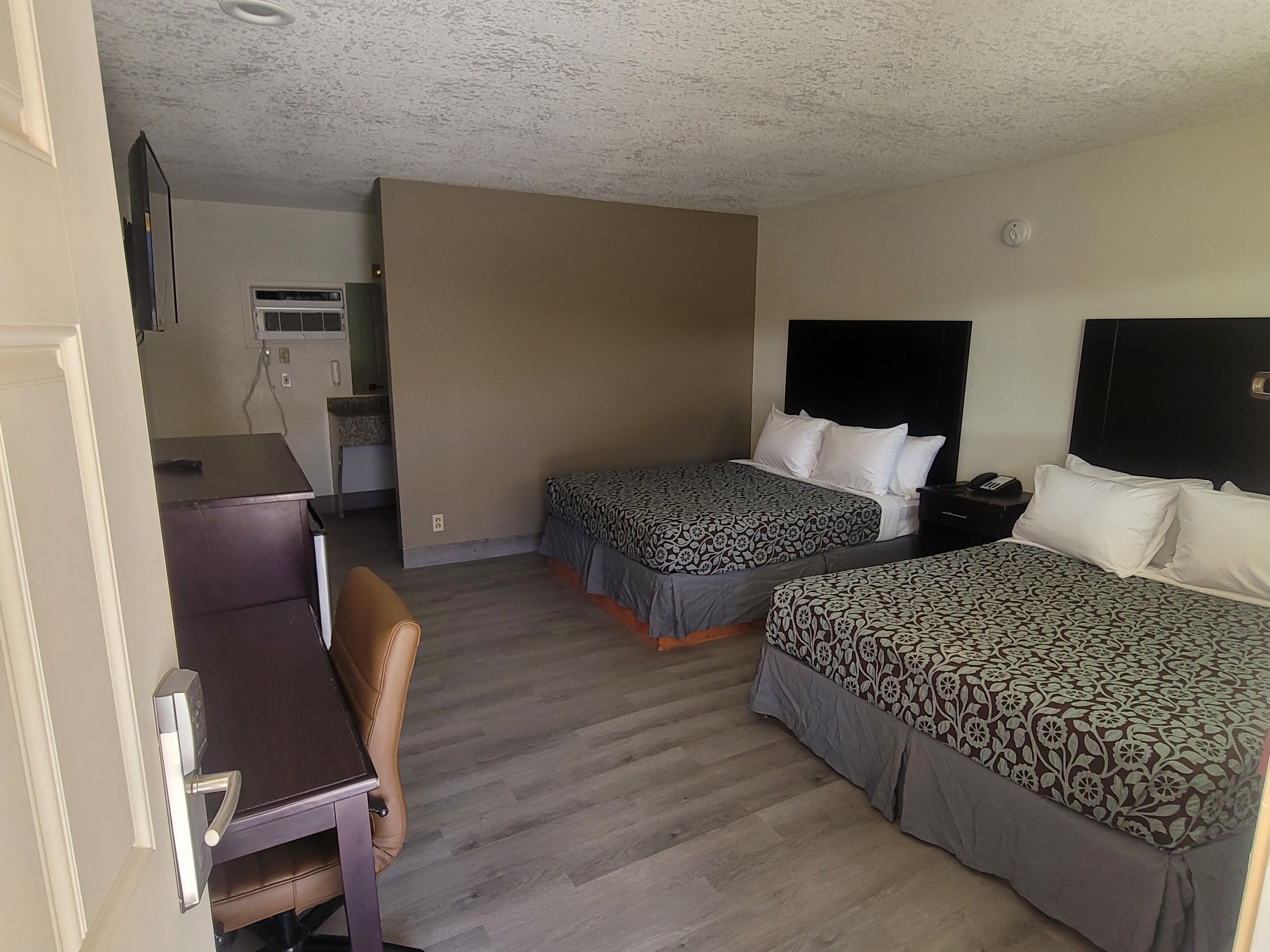 Ein Hotelzimmer mit zwei Betten, einem Schreibtisch, einem Stuhl und einer Küchenzeile.