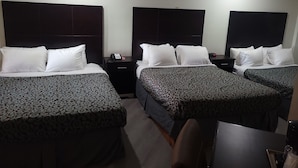A hotel room with three beds, each with a patterned bedspread and white pillows. There is a bedside table with a phone and a small lamp. The room has a simple, functional design with a plain wall and a ceiling light. - Econo Lodge Las Vegas NM (Las Vegas)