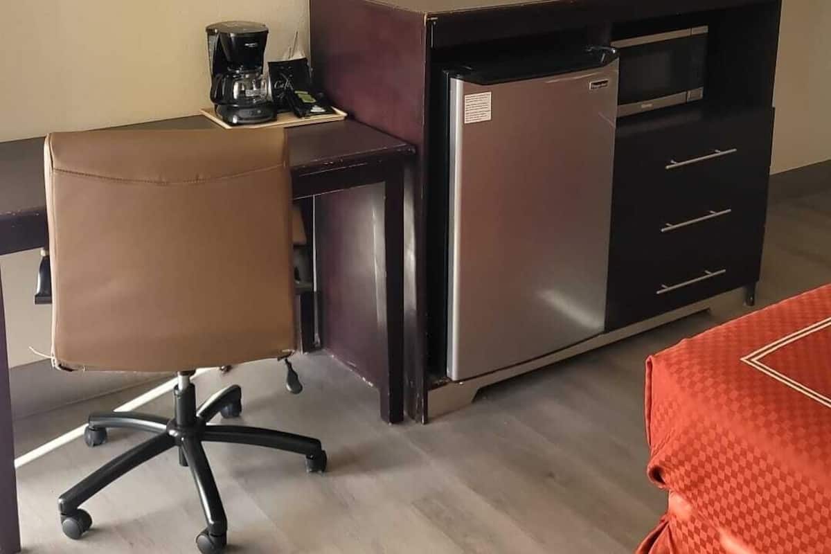 Une chambre d’hôtel compacte comprenant un lit, un bureau avec une chaise, un réfrigérateur et un téléviseur à écran plat fixé au mur.